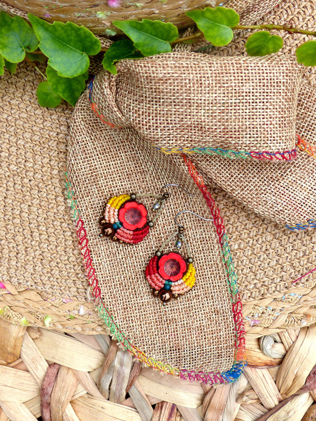 Peut inclure: Une paire de boucles d'oreilles en crochet colorées avec des accents rouges, orange, jaunes, verts et bleus. Les boucles d'oreilles sont suspendues à un morceau de tissu de jute avec un bord tissé.