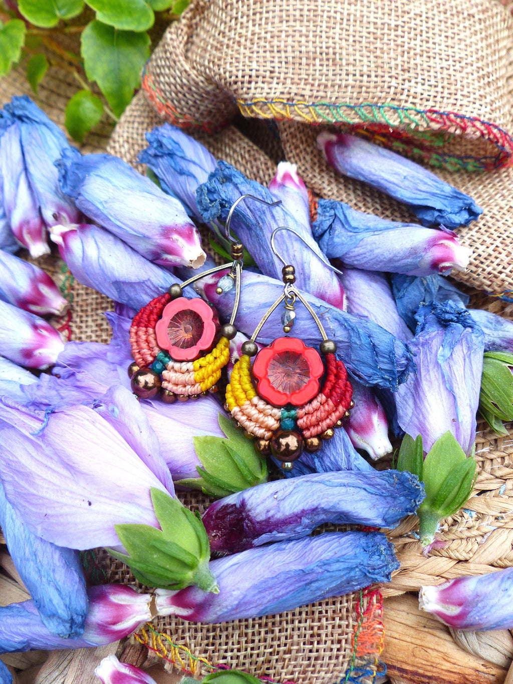 Peut inclure: Une paire de boucles d'oreilles colorées et faites à la main avec un schéma de couleurs rouge, orange, jaune et vert. Les boucles d'oreilles sont en macramé et présentent un petit charme de fleur rouge.