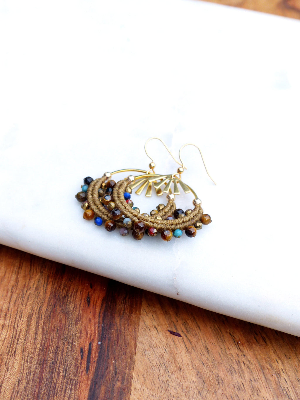 Peut inclure: Une paire de boucles d'oreilles créoles dorées avec un cordon brun enroulé autour du cercle et rehaussé de perles colorées. Les perles sont un mélange de brun, bleu, vert et rouge.