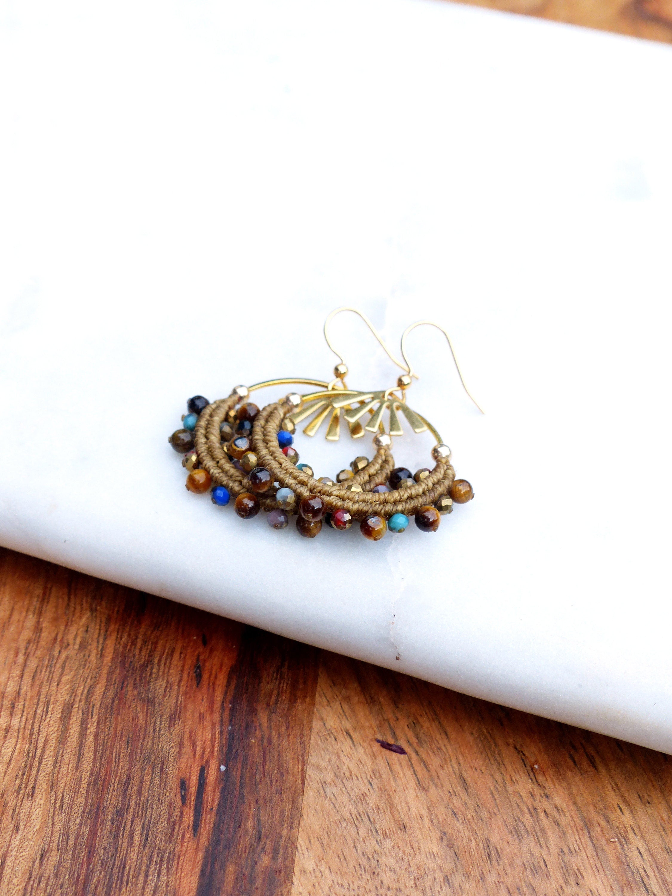 Peut inclure: Une paire de boucles d'oreilles créoles dorées avec un cordon brun enroulé autour du cercle et rehaussé de perles colorées. Les perles sont un mélange de brun, bleu, vert et rouge.