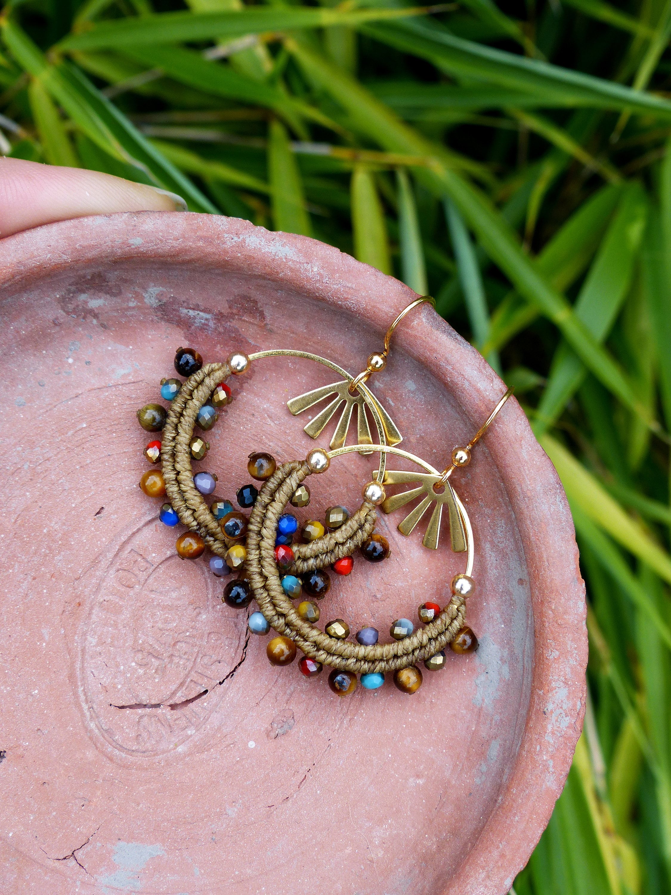 Peut inclure: Une paire de boucles d'oreilles créoles dorées avec du macramé marron et des perles colorées. Les perles sont un mélange d'œil de tigre, de bleu, de rouge et d'or.