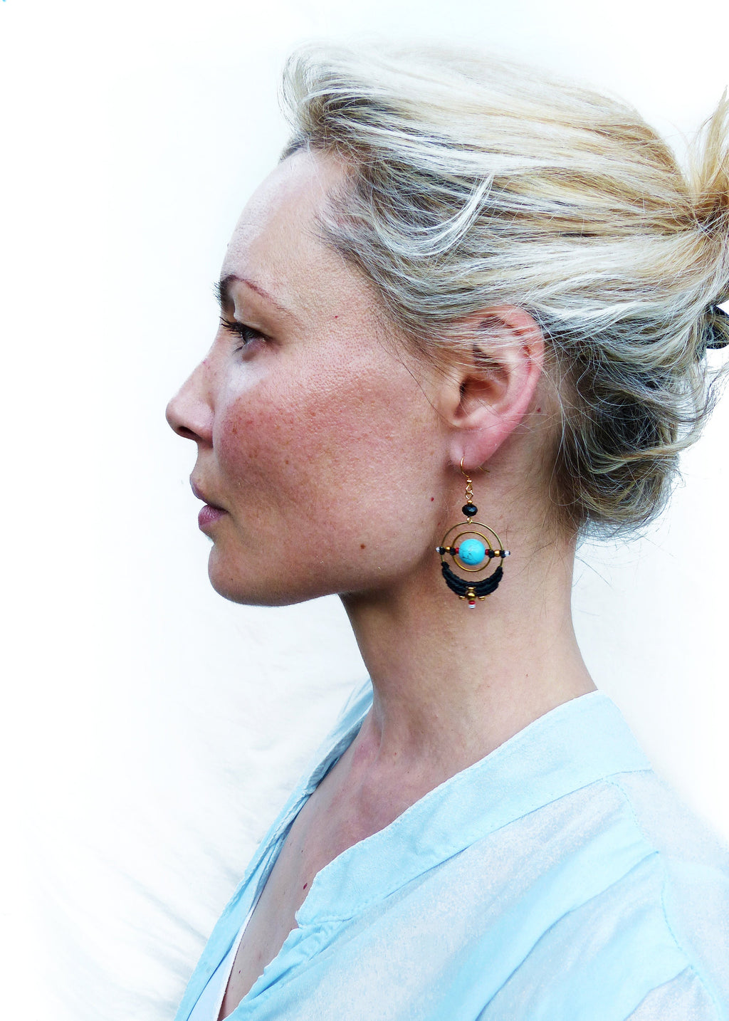 Peut inclure: Une femme portant une chemise bleu clair avec une paire de boucles d'oreilles pendantes. Les boucles d'oreilles sont faites de cordon noir, de fil d'or et d'une pierre turquoise.