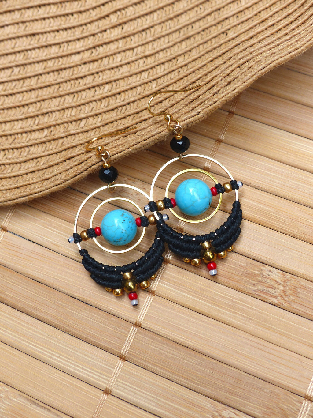 Peut inclure: Une paire de boucles d'oreilles créoles turquoise et noires avec des accents dorés. Les boucles d'oreilles présentent une pierre turquoise au centre de chaque créole, entourée de perles noires et d'accents dorés.
