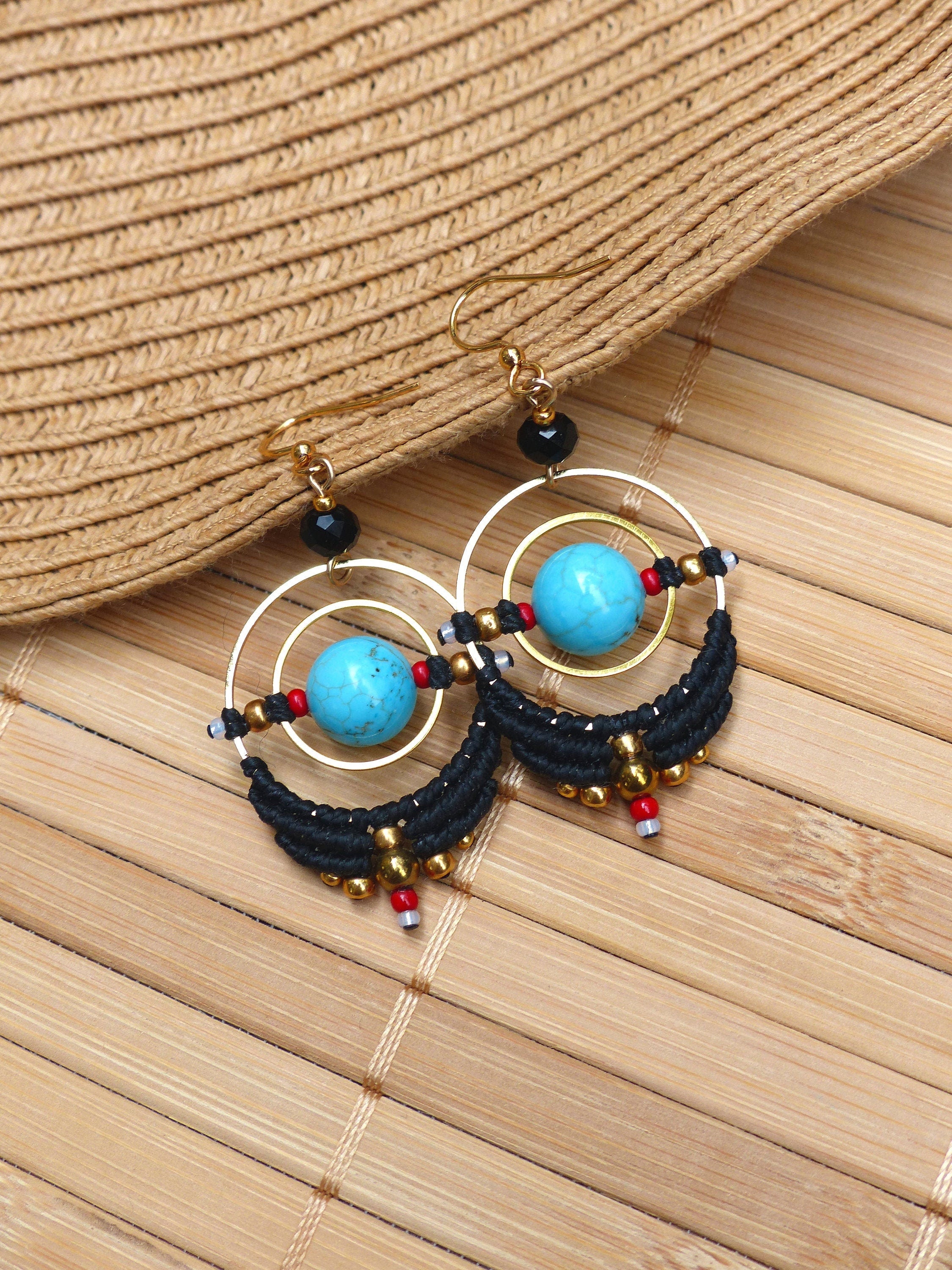 Peut inclure: Une paire de boucles d'oreilles créoles turquoise et noires avec des accents dorés. Les boucles d'oreilles présentent une pierre turquoise au centre de chaque créole, entourée de perles noires et d'accents dorés.