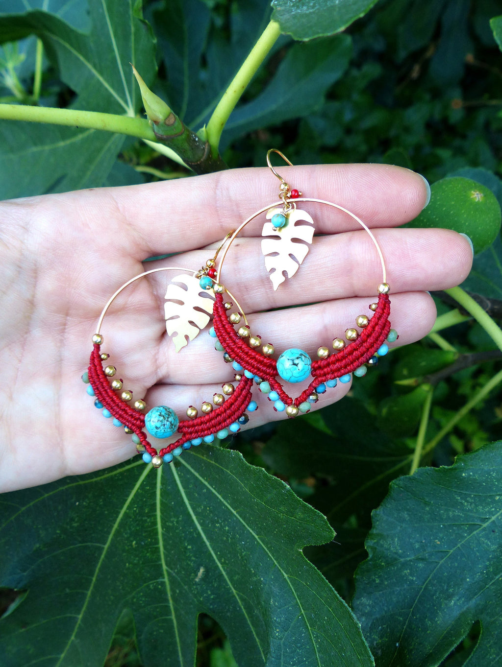 Peut inclure: Boucles d'oreilles créoles rouges et dorées avec des perles turquoise et un pendentif en forme de feuille dorée. Les boucles d'oreilles sont faites à la main et présentent un design en macramé.
