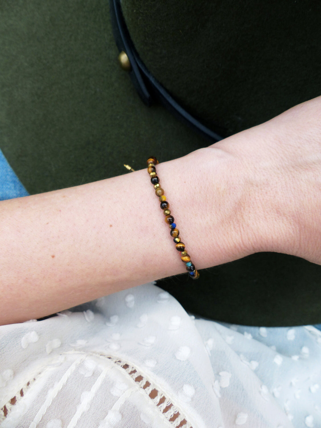 Peut inclure: Un bracelet en or avec des perles brunes, noires et bleues. Le bracelet est porté au poignet.