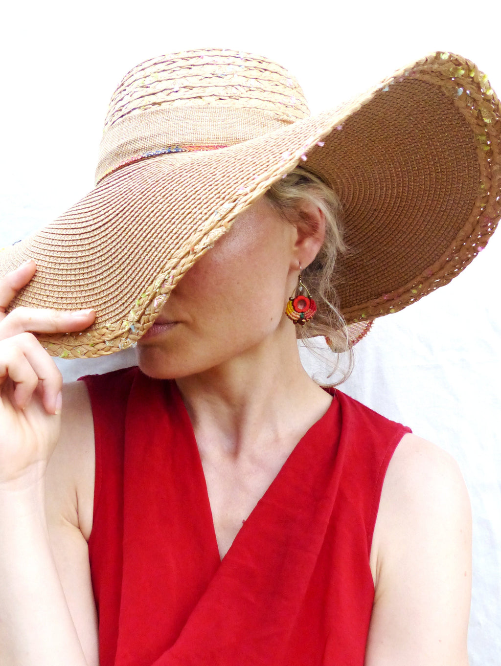 Peut inclure: Une femme portant un chapeau de paille à larges bords avec une boucle d'oreille en perles rouge et orange. Elle porte une robe rouge sans manches.