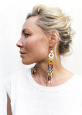Peut inclure: Une paire de longues boucles d'oreilles en perles colorées avec un pendentif rond blanc. Les boucles d'oreilles sont faites avec une variété de perles dans des tons de rouge, orange, jaune, vert, bleu et violet. Les perles sont enfilées sur un fil fin et pendent en cascade.