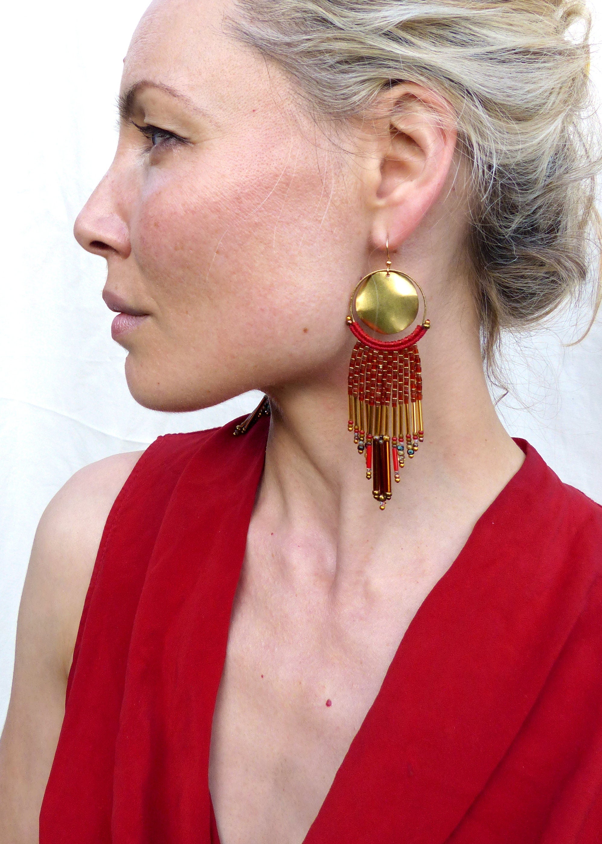 Peut inclure: Une paire de boucles d'oreilles pendantes dorées et rouges avec un grand disque rond doré et une frange de perles rouges.