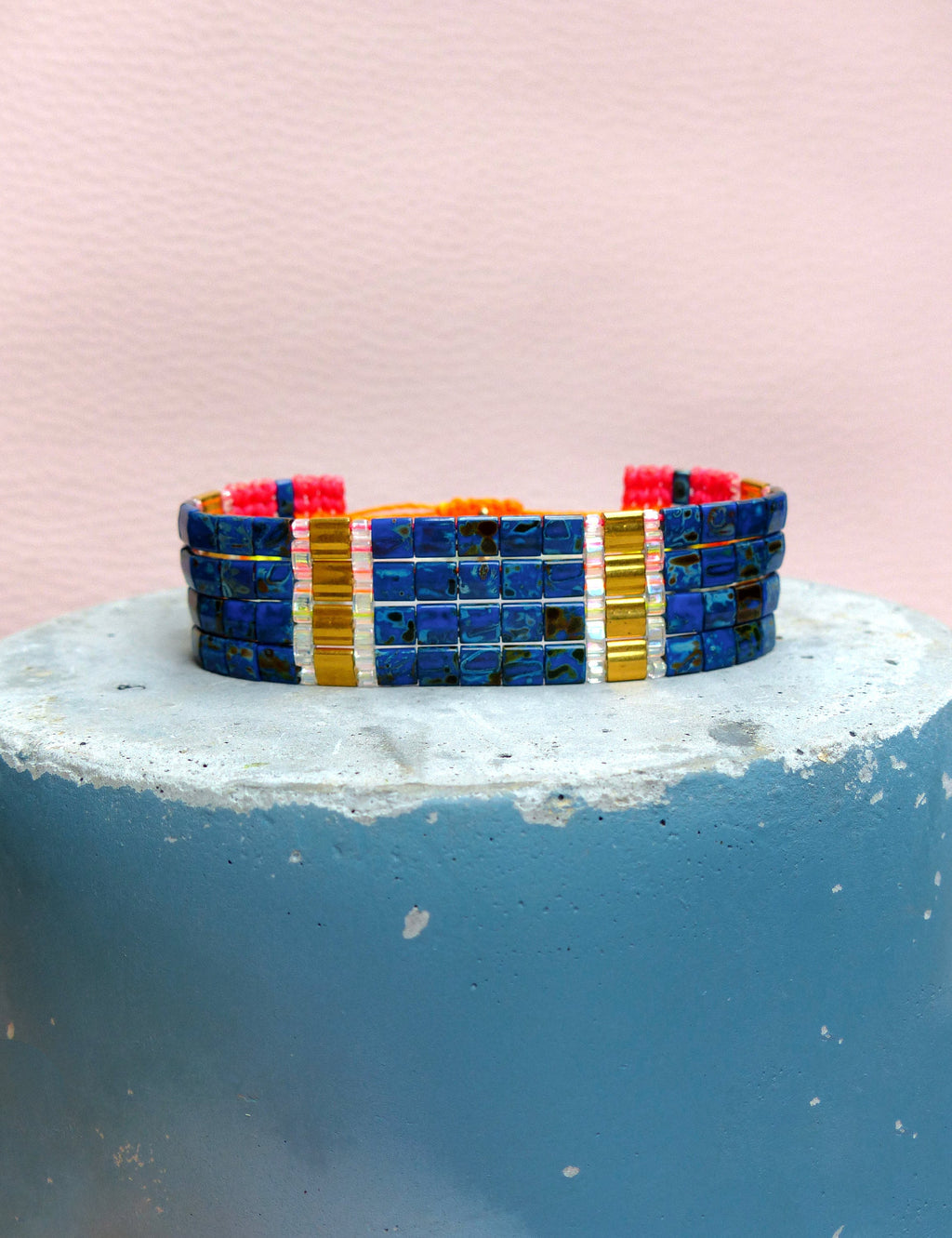 Peut inclure: Un bracelet en perles bleues et dorées avec des accents roses. Le bracelet est composé de petites perles carrées et est empilé sur plusieurs rangées.