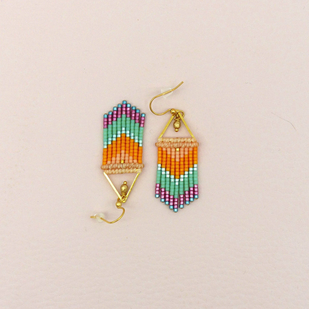 Peut inclure: Une paire de boucles d'oreilles perlées avec un motif géométrique. Les boucles d'oreilles présentent une combinaison de perles orange, turquoise, rose et beige. Les boucles d'oreilles sont suspendues à des crochets dorés.