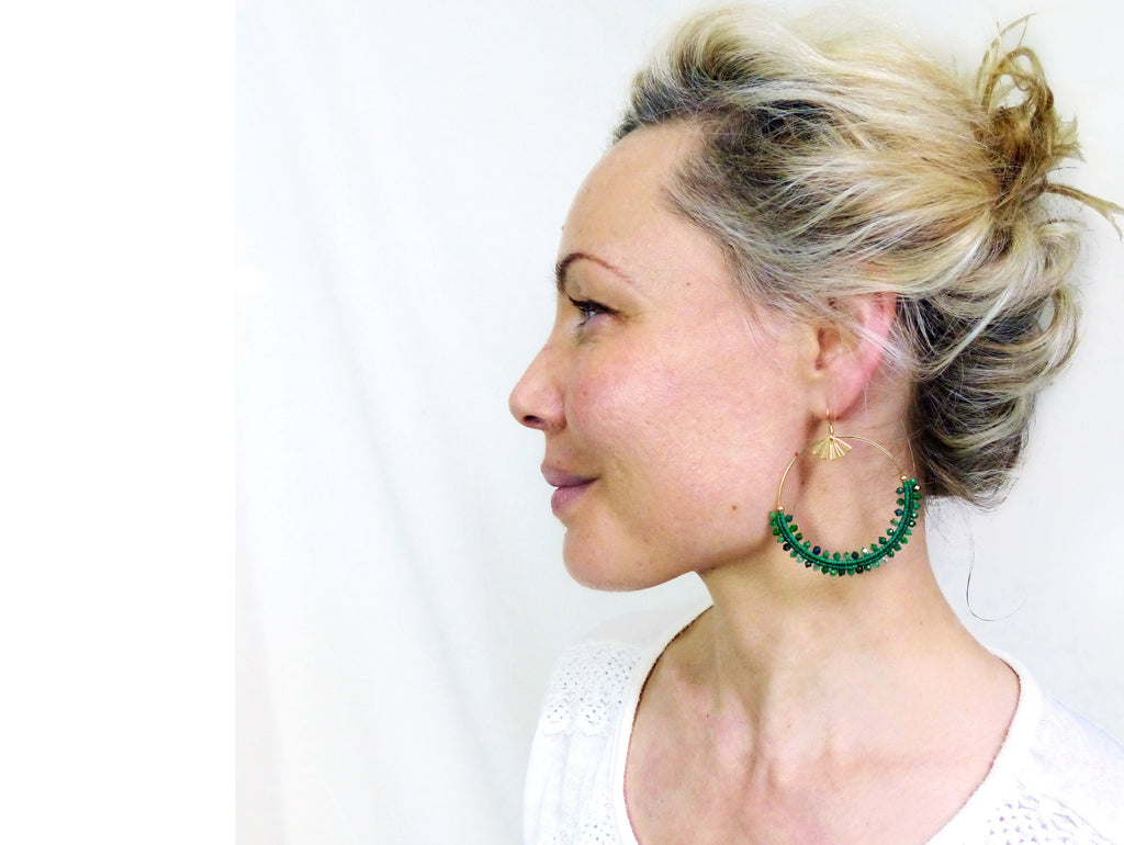 Peut inclure: Une paire de boucles d'oreilles créoles en perles vertes avec un charme en forme d'éventail doré suspendu à l'une des boucles d'oreilles.
