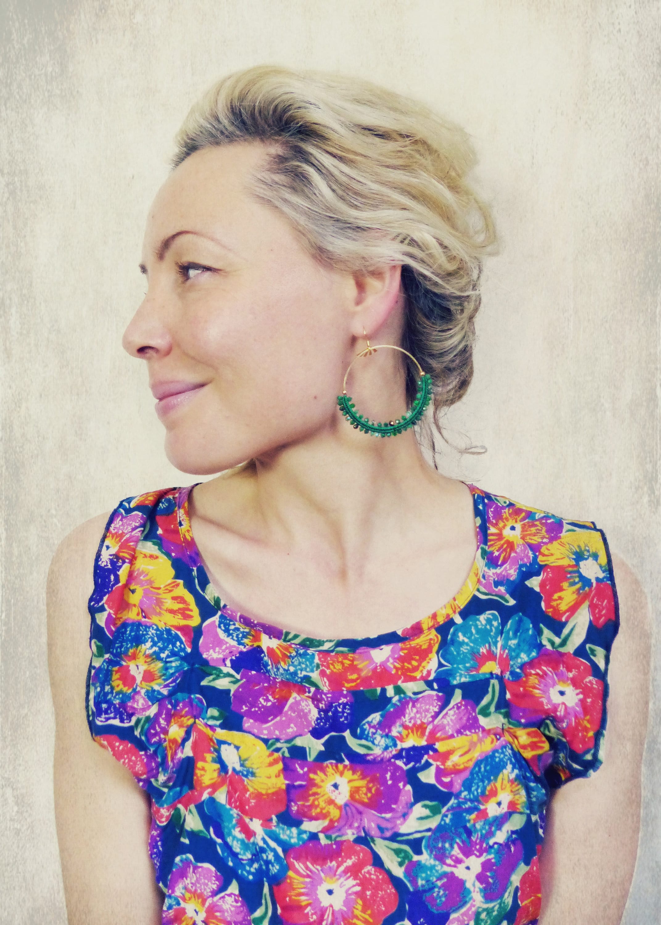 Peut inclure: Une femme aux cheveux blonds portant une robe à imprimé floral et de grandes boucles d'oreilles en forme de cerceau ornées de perles vertes.