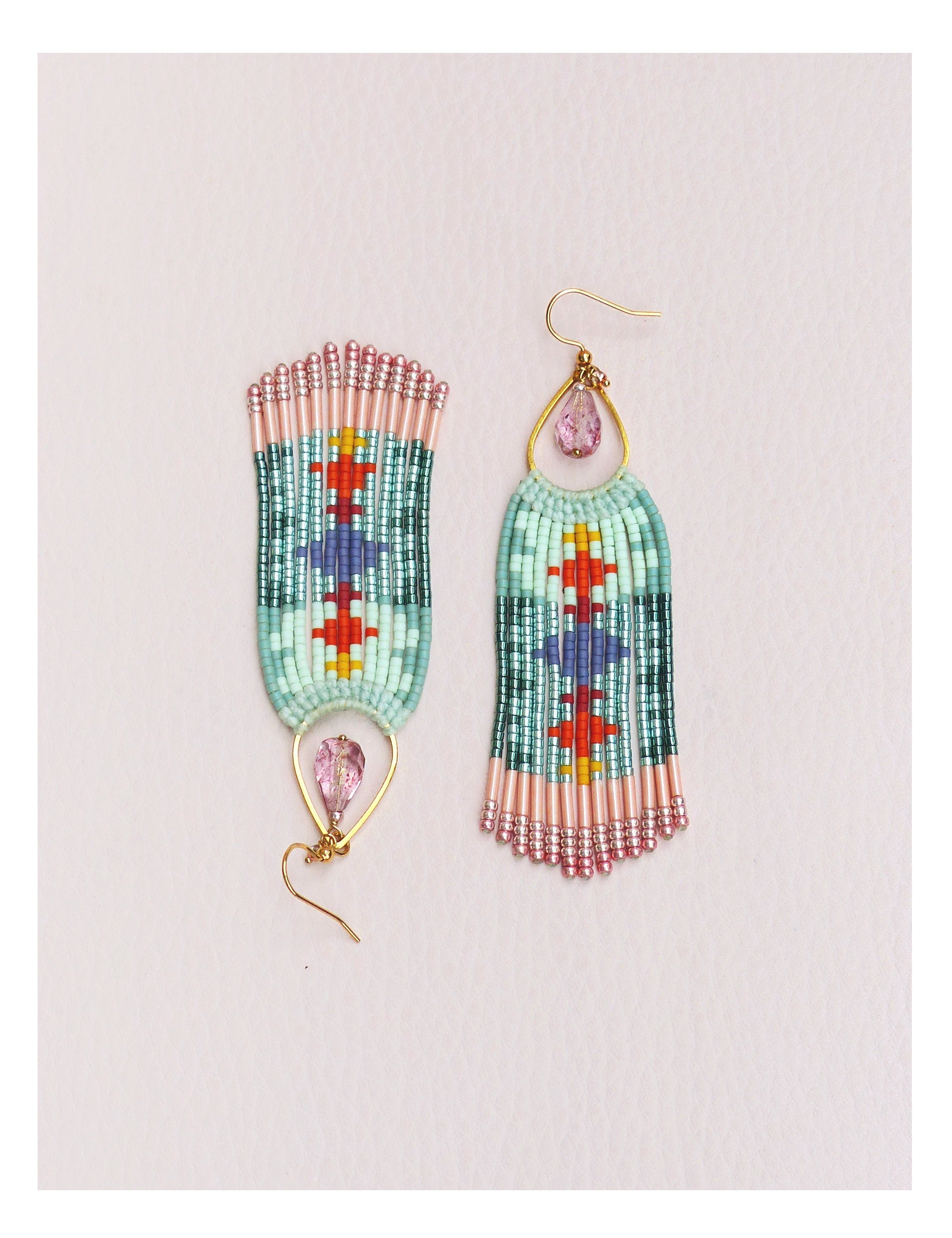 Peut inclure: Une paire de boucles d'oreilles perlées avec un motif géométrique. Les boucles d'oreilles présentent une combinaison de perles bleu clair, roses, rouges et violettes. Chaque boucle d'oreille a un crochet doré et une gemme rose en forme de goutte.