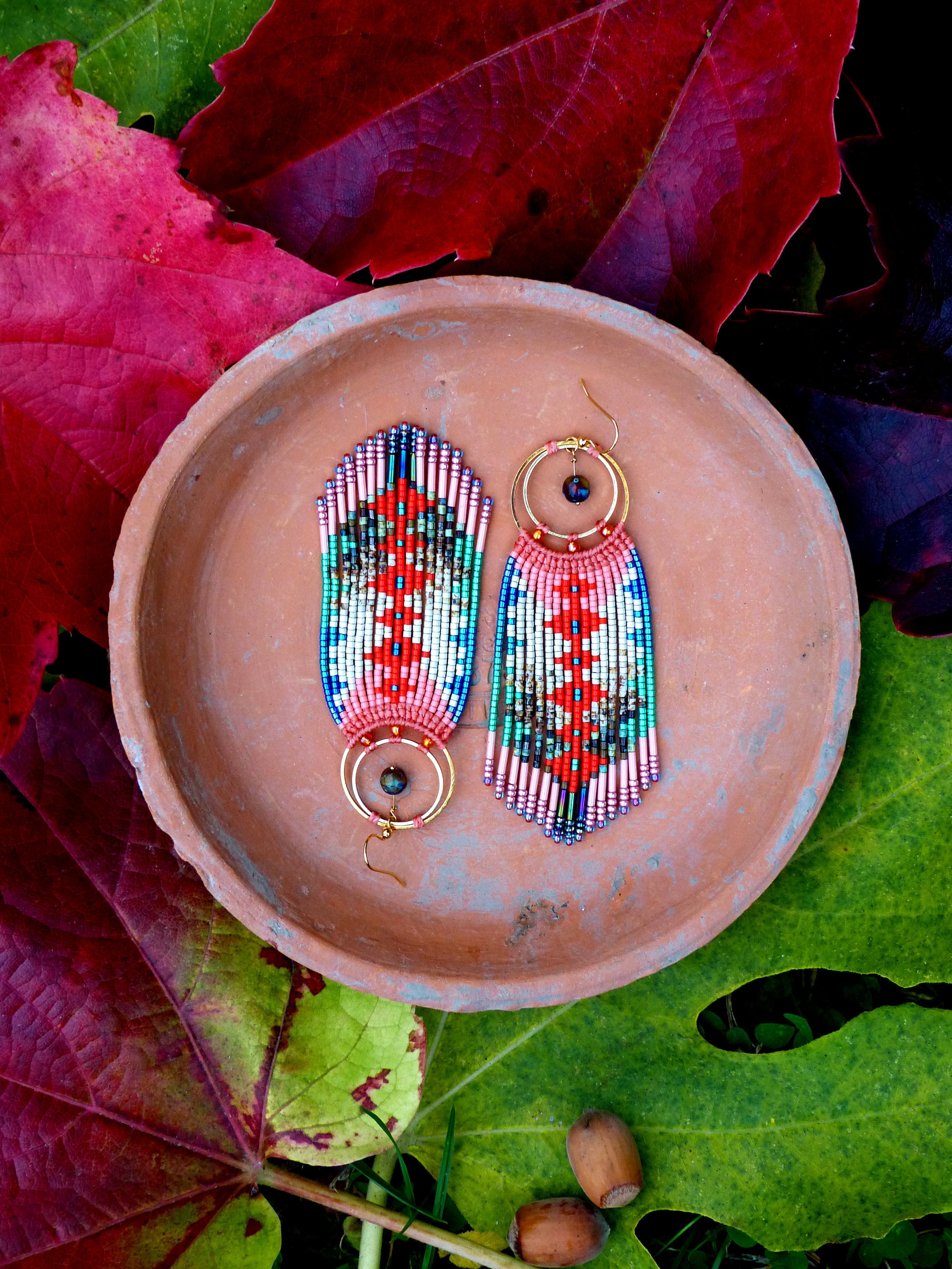 Peut inclure: Une paire de longues boucles d'oreilles en perles colorées avec un motif géométrique. Les boucles d'oreilles sont faites avec une variété de perles dans des tons de rose, bleu, vert et blanc. Les boucles d'oreilles sont suspendues à des créoles dorées avec une perle bleu foncé au sommet de chaque créole.