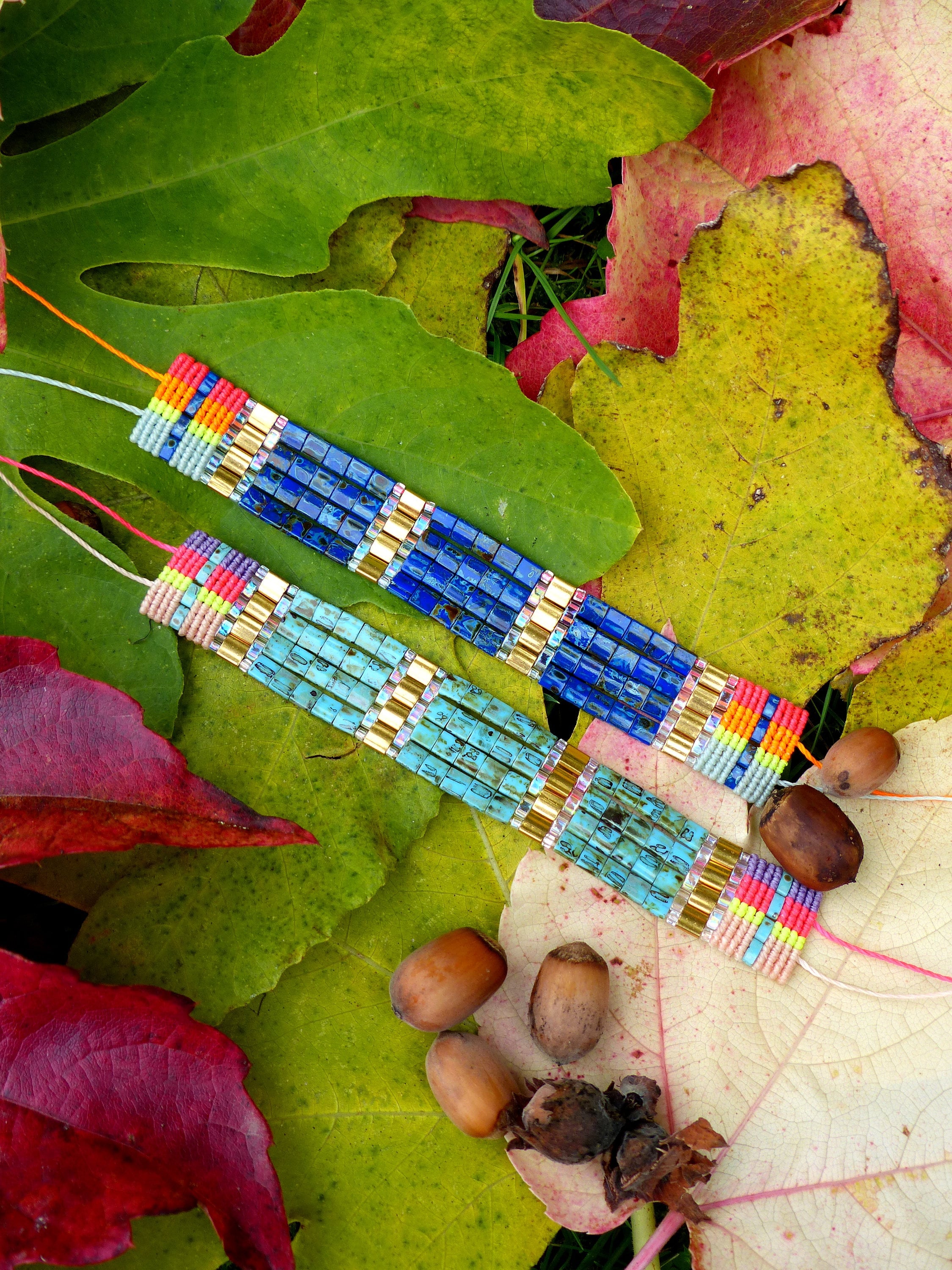 Peut inclure: Deux bracelets en perles avec du fil coloré et des accents dorés. Les bracelets sont sur un lit de feuilles d'automne.
