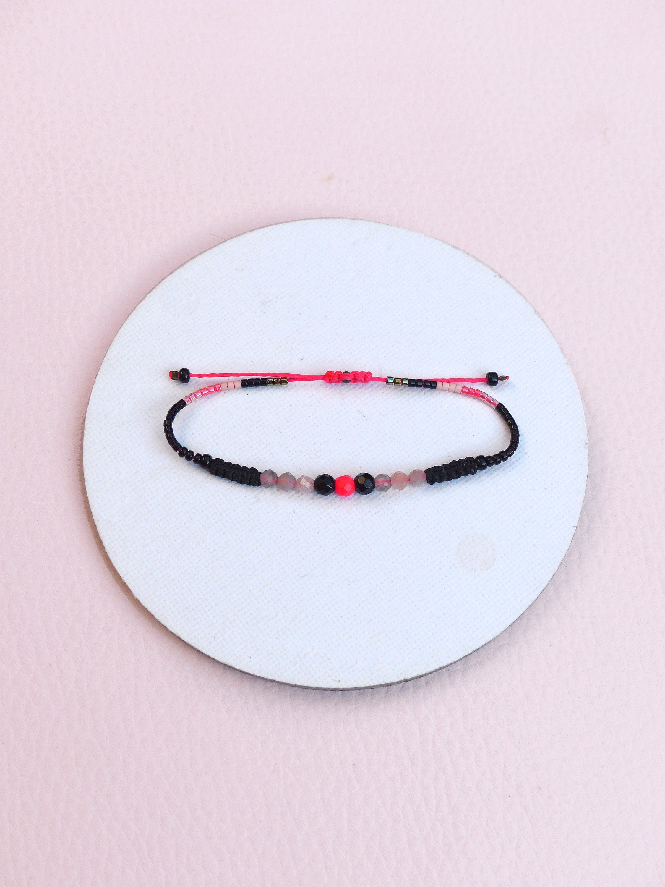 Peut inclure: Un bracelet en perles noires et roses avec une perle rouge au centre.