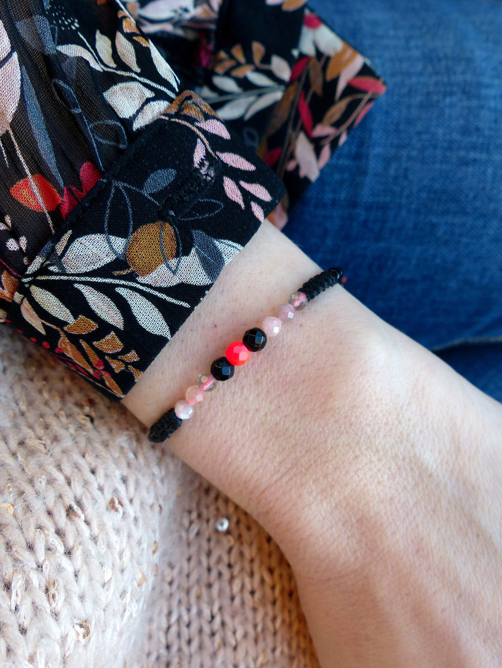Peut inclure: Un bracelet en cordon noir avec des perles roses, rouges et noires. Le bracelet est porté au poignet.
