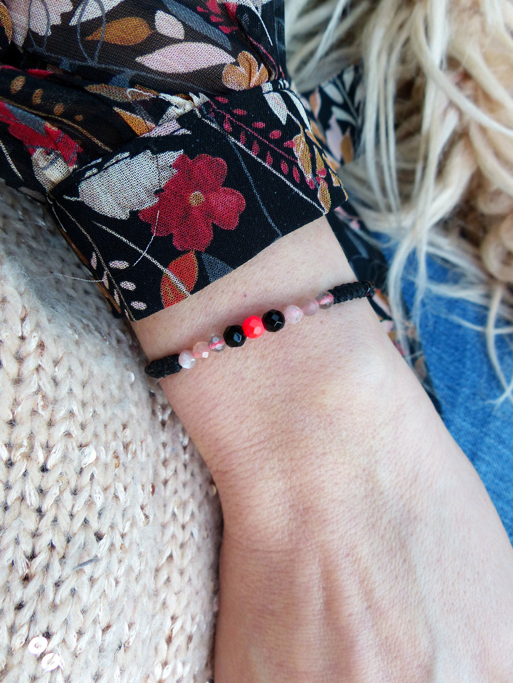 Peut inclure: Un bracelet en cordon noir avec des perles roses, noires et rouges. Le bracelet est porté au poignet.