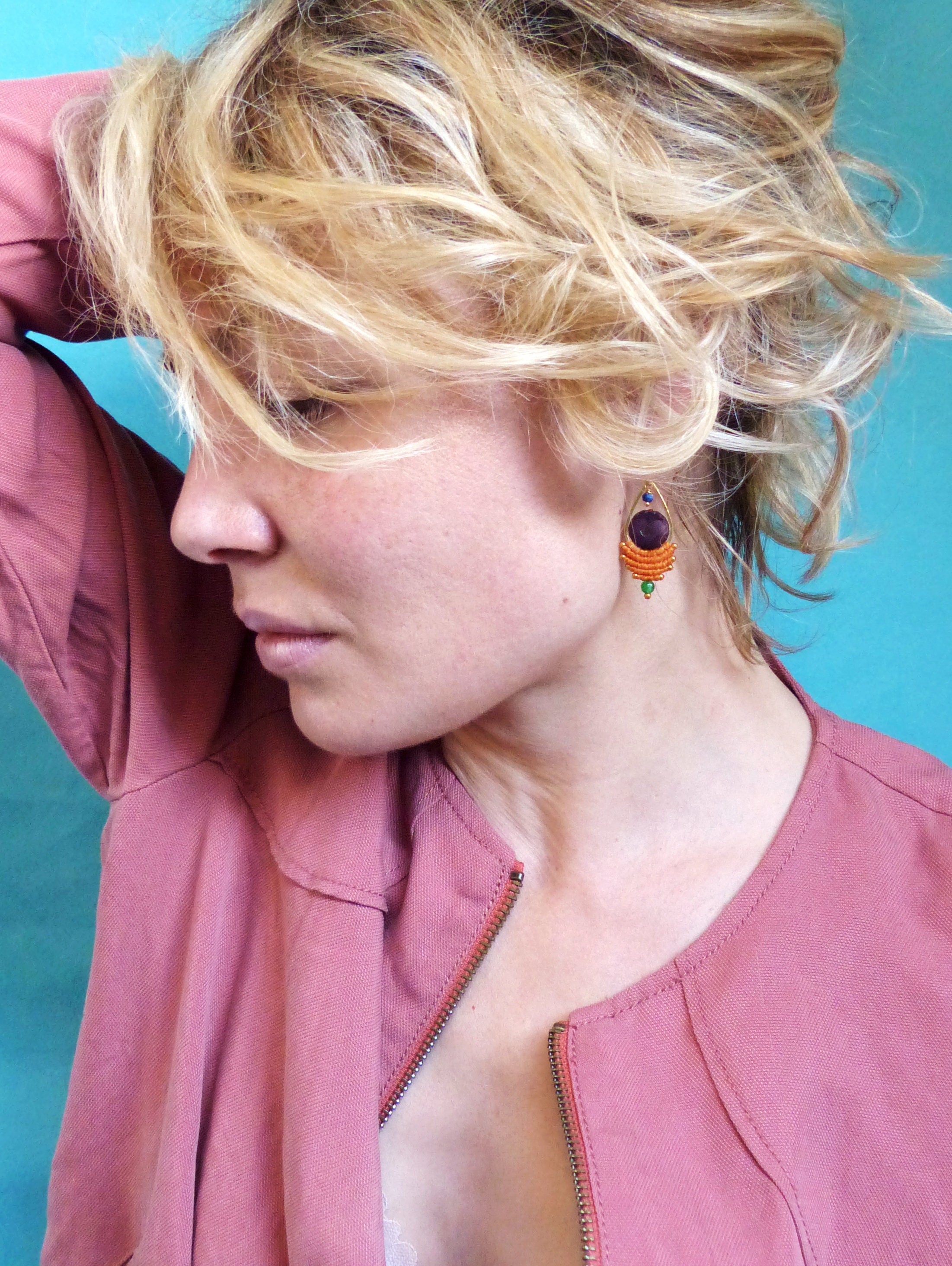 Peut inclure: Une femme aux cheveux blonds portant une veste rose et des boucles d'oreilles avec des perles violettes, orange et vertes.