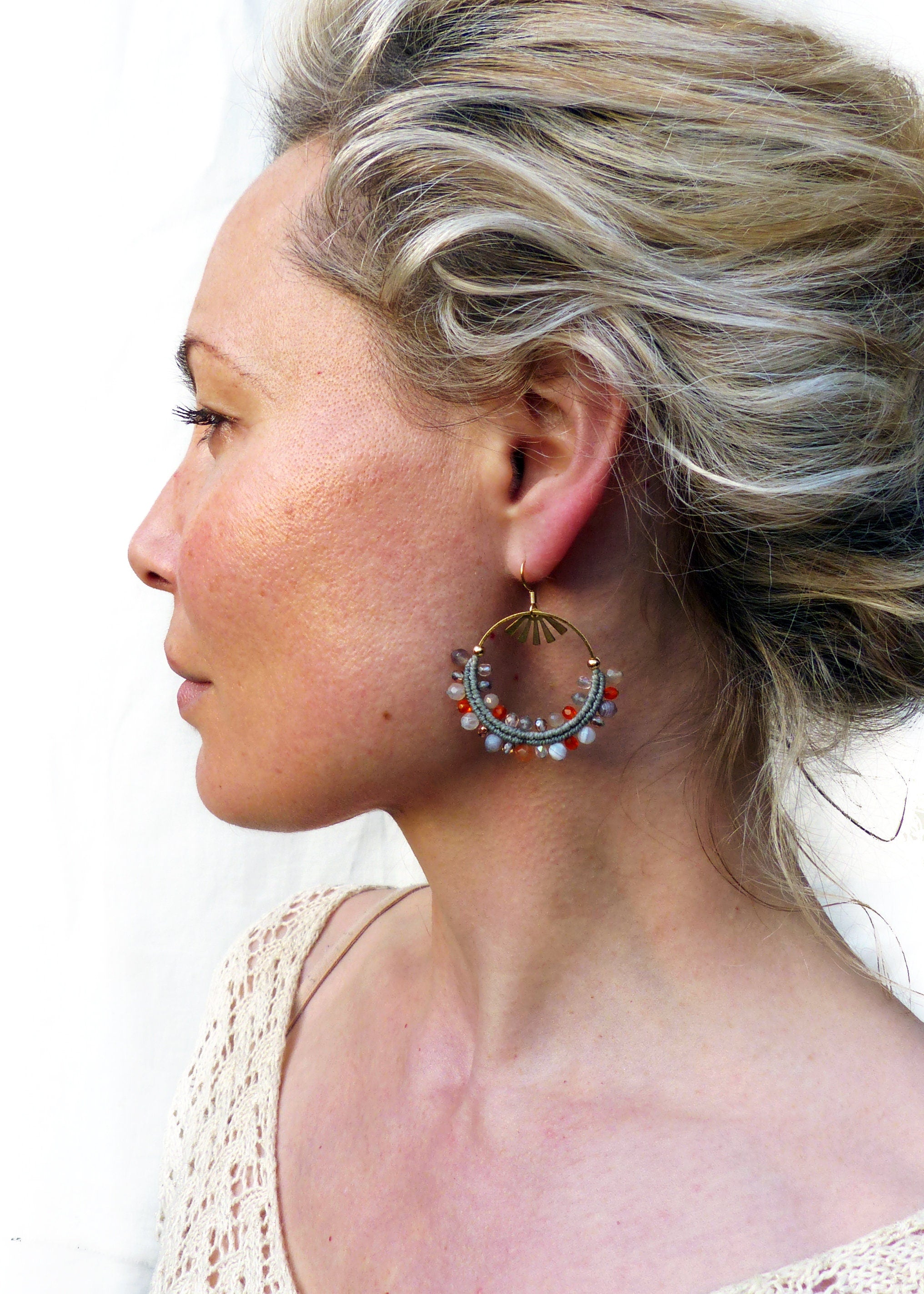 Peut inclure: Une femme portant une paire de boucles d'oreilles créoles dorées avec un design perlé. Les perles sont dans des tons de gris, orange et blanc.