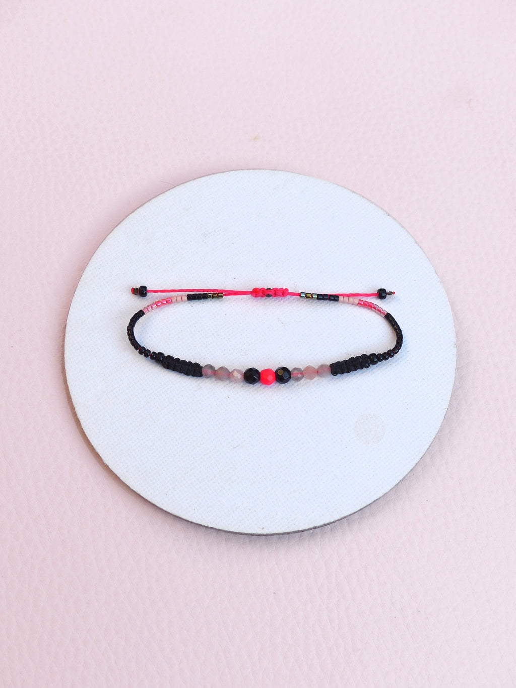 Peut inclure: Un bracelet en perles noires et roses avec une perle rouge au centre.