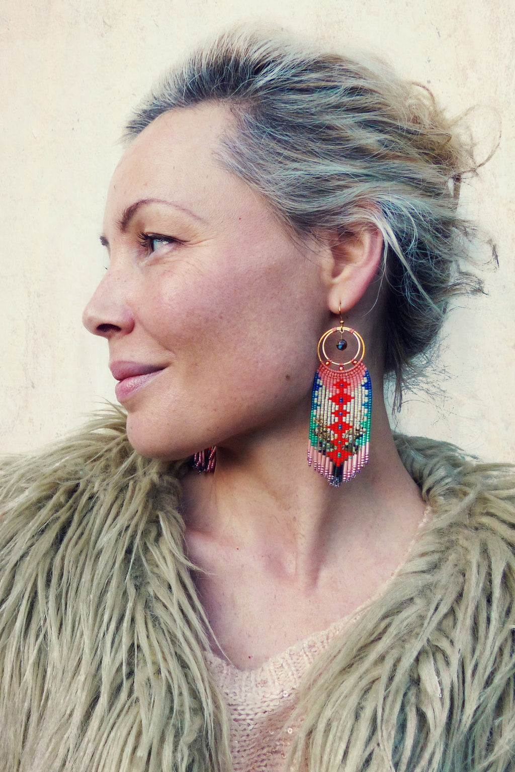 Peut inclure: Une femme portant une veste en fausse fourrure marron clair avec une paire de longues boucles d'oreilles en perles colorées. Les boucles d'oreilles sont faites de petites perles colorées et ont un anneau en or en haut. Les boucles d'oreilles pendent jusqu'aux épaules de la femme.