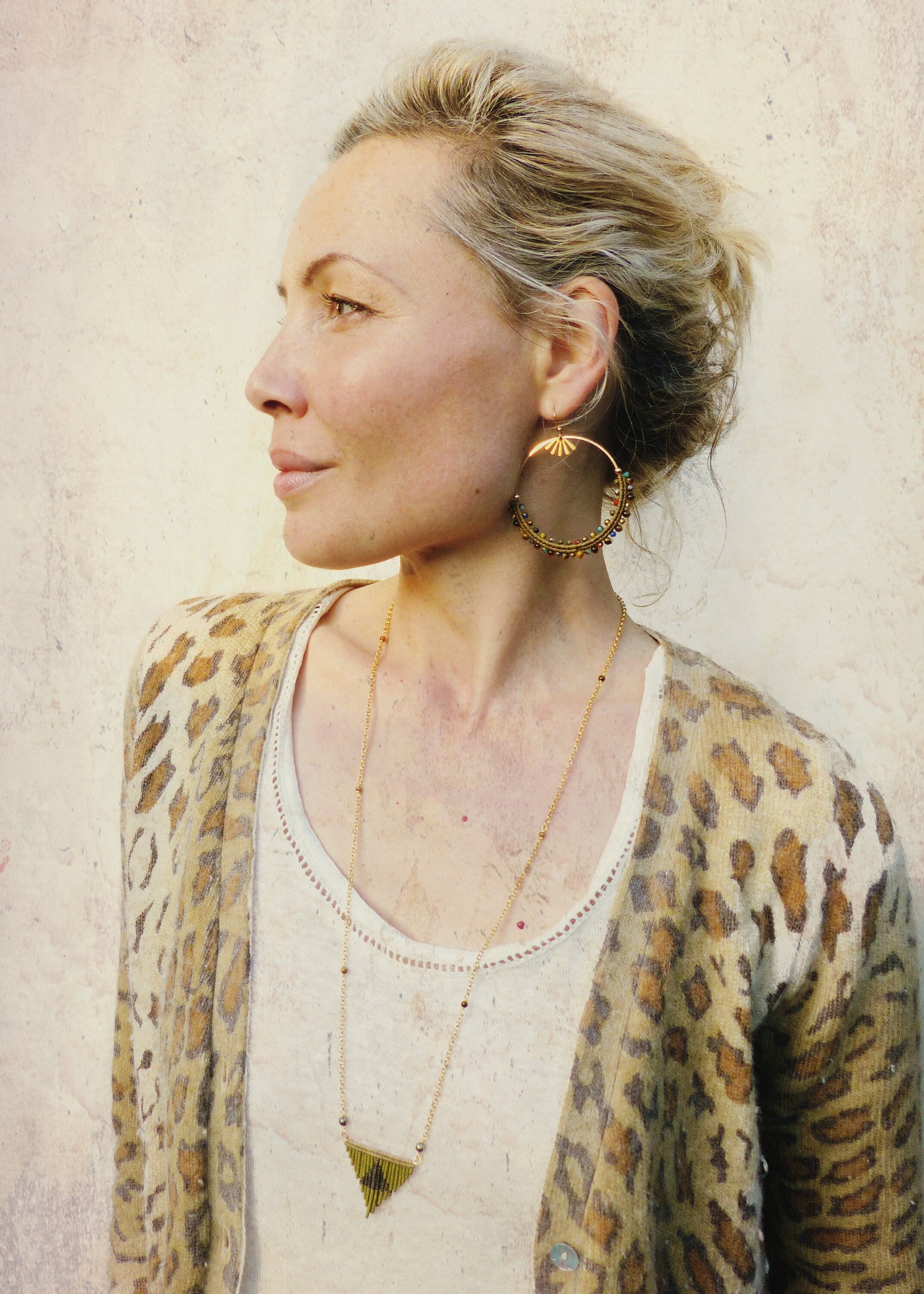 Peut inclure: Une femme portant un cardigan léopard avec un collier en or et de grandes boucles d'oreilles créoles dorées avec des perles colorées.