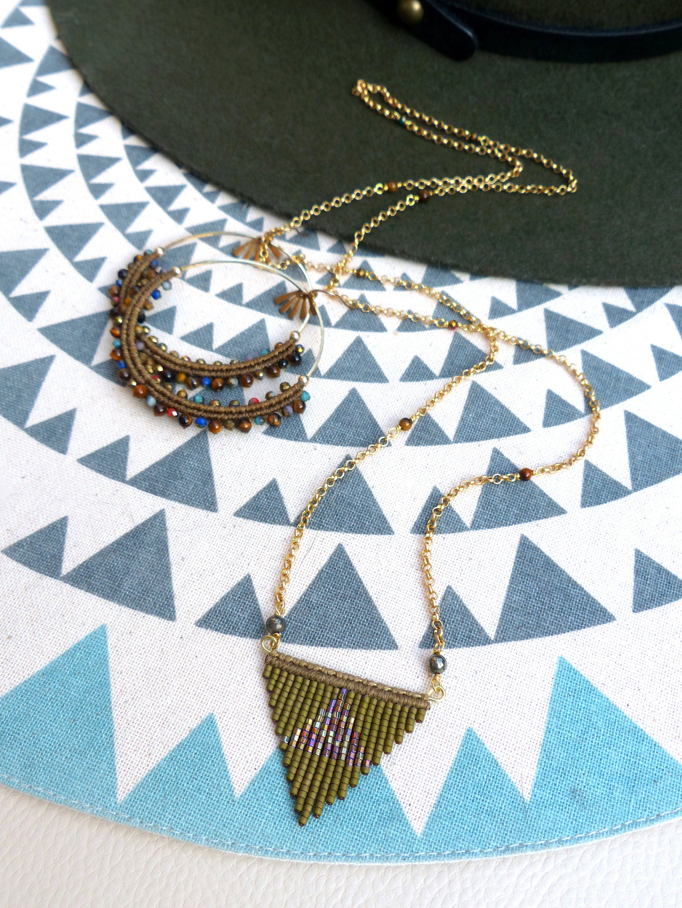 Peut inclure: Deux colliers en or avec des pendentifs en perles brunes et multicolores. Les colliers sont sur un fond de tissu à motifs blancs et bleus.