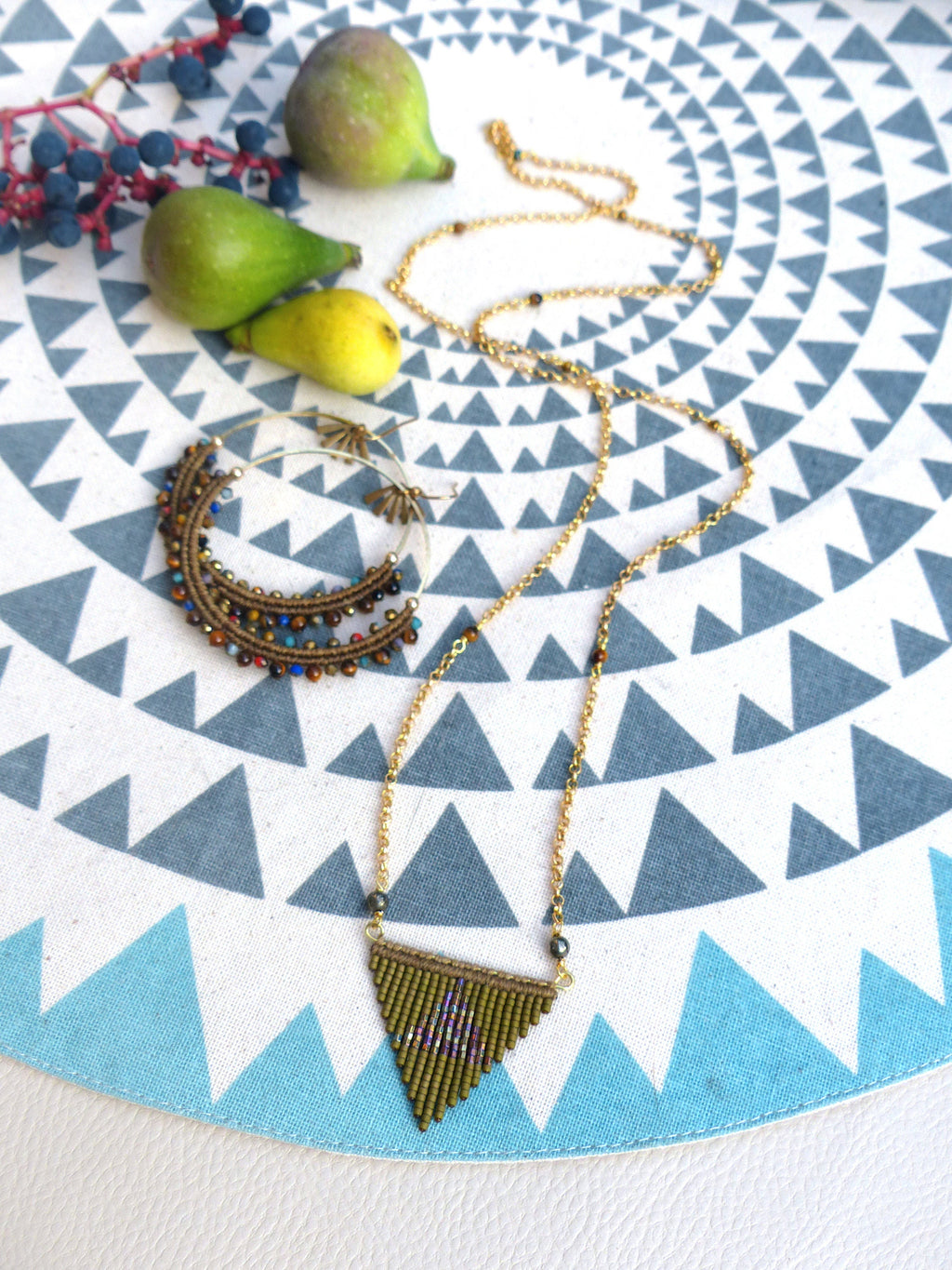 Peut inclure: Un collier en chaîne dorée avec un pendentif triangulaire en perles brunes. Le pendentif est un motif géométrique avec une frange de perles. Le collier est sur un fond blanc avec un motif bleu et blanc.
