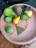 Peut inclure: Un collier de perles vertes et brunes avec un pendentif triangulaire est suspendu à une assiette en terre cuite avec des figues vertes et une petite grappe de baies bleues. L'assiette porte un tampon qui indique "Établi depuis 1875."