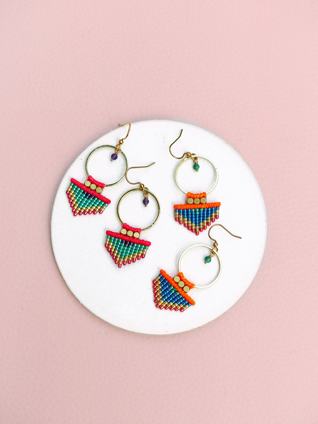 Peut inclure: Trois paires de boucles d'oreilles créoles dorées avec des franges de perles colorées. Les franges sont composées de petites perles colorées dans des tons de rose, orange, vert et bleu. Les créoles sont simples et élégantes.