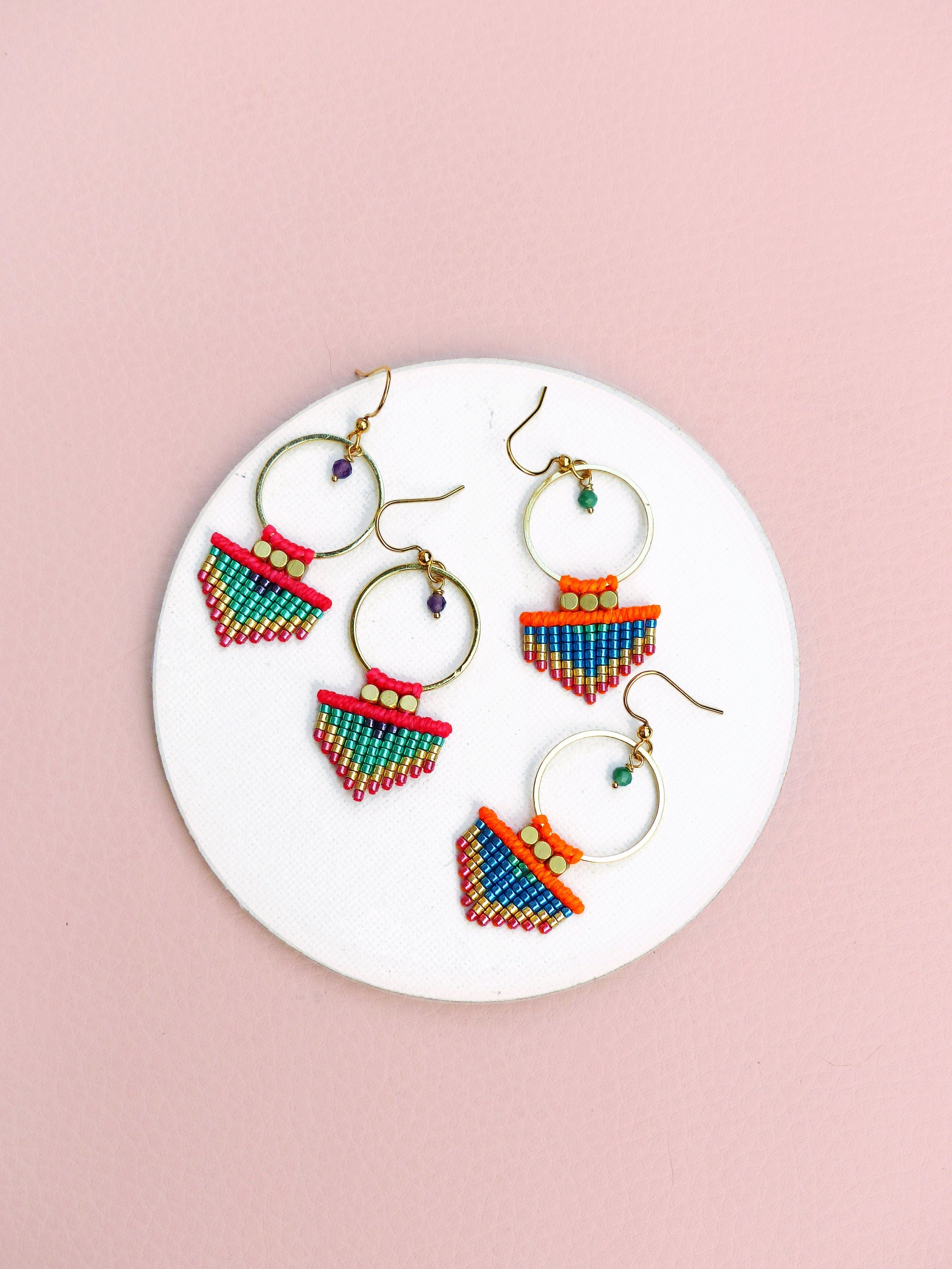 Peut inclure: Trois paires de boucles d'oreilles créoles dorées avec des franges de perles colorées. Les franges sont composées de petites perles colorées dans des tons de rose, orange, vert et bleu. Les créoles sont simples et élégantes.