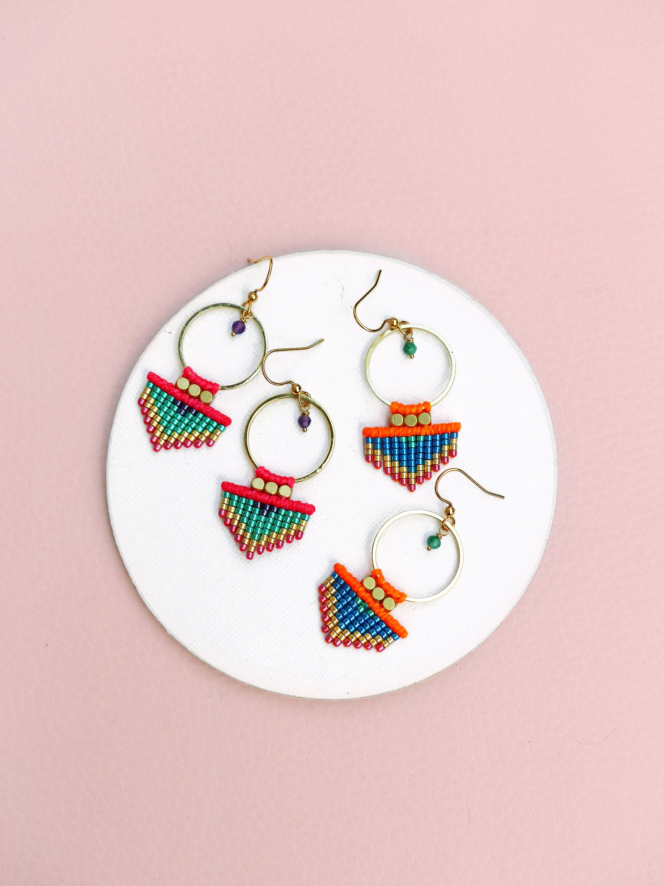 Peut inclure: Trois paires de boucles d'oreilles créoles dorées avec des franges de perles colorées. Les franges sont composées de petites perles colorées dans des tons de rose, orange, vert et bleu. Les créoles sont simples et élégantes.