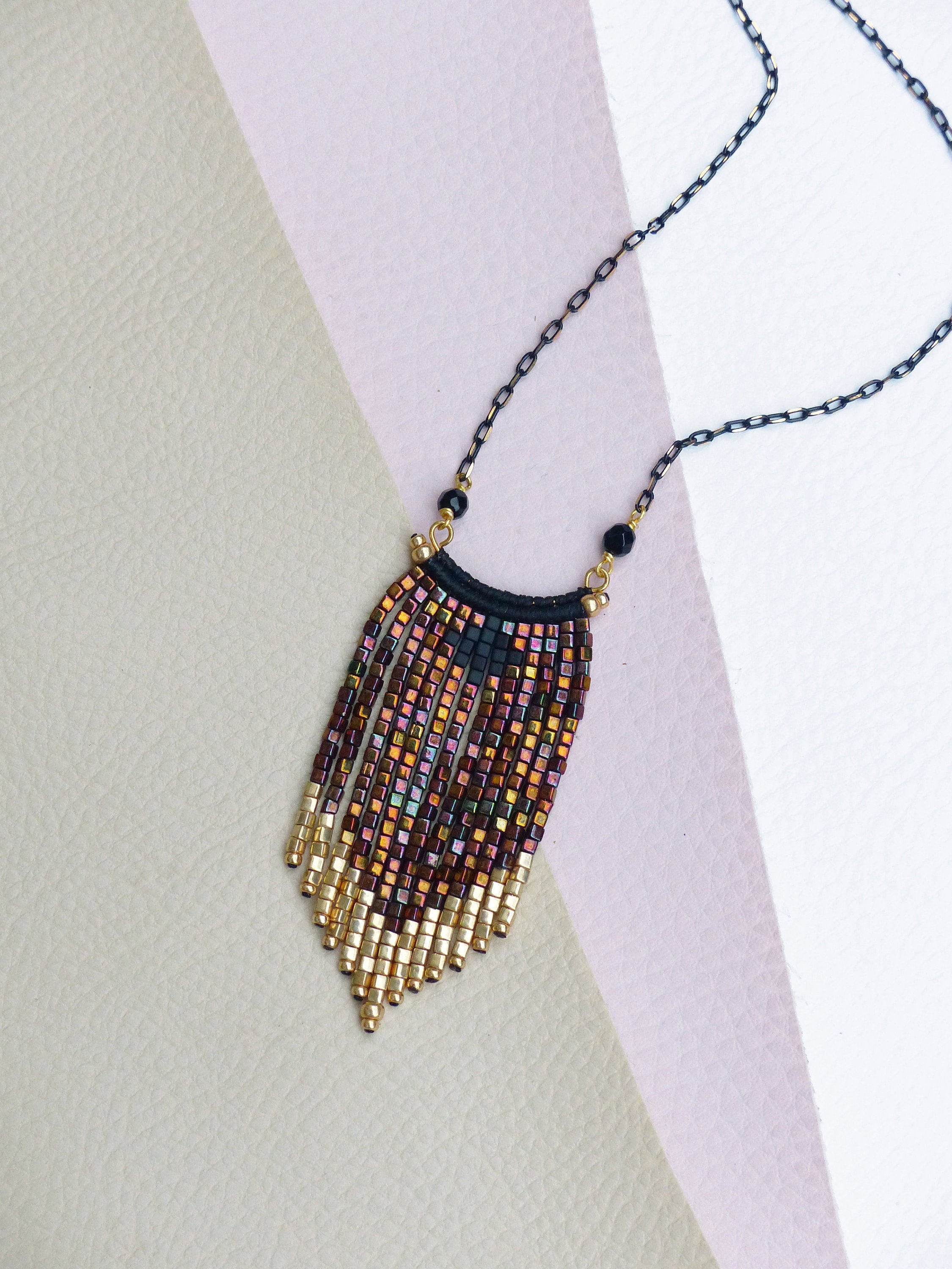 Peut inclure: Un collier de perles dorées et brunes avec une chaîne noire. Les perles sont disposées en un motif gradué, créant un effet de frange.