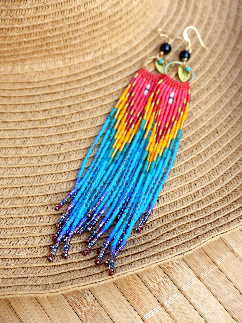 Peut inclure: Une paire de longues boucles d'oreilles en perles colorées avec des accents dorés. Les boucles d'oreilles sont faites de perles rouges, orange, jaunes, bleues et violettes. Les boucles d'oreilles sont suspendues à des crochets dorés avec des perles noires en haut.