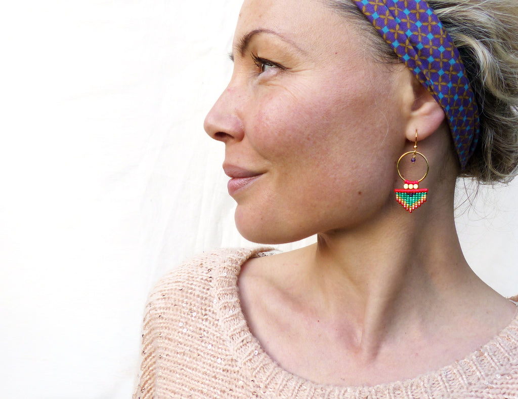 Peut inclure: Une femme portant un bandeau à motif géométrique et une paire de boucles d'oreilles en perles rouges, vertes et dorées avec un design de cerceau.