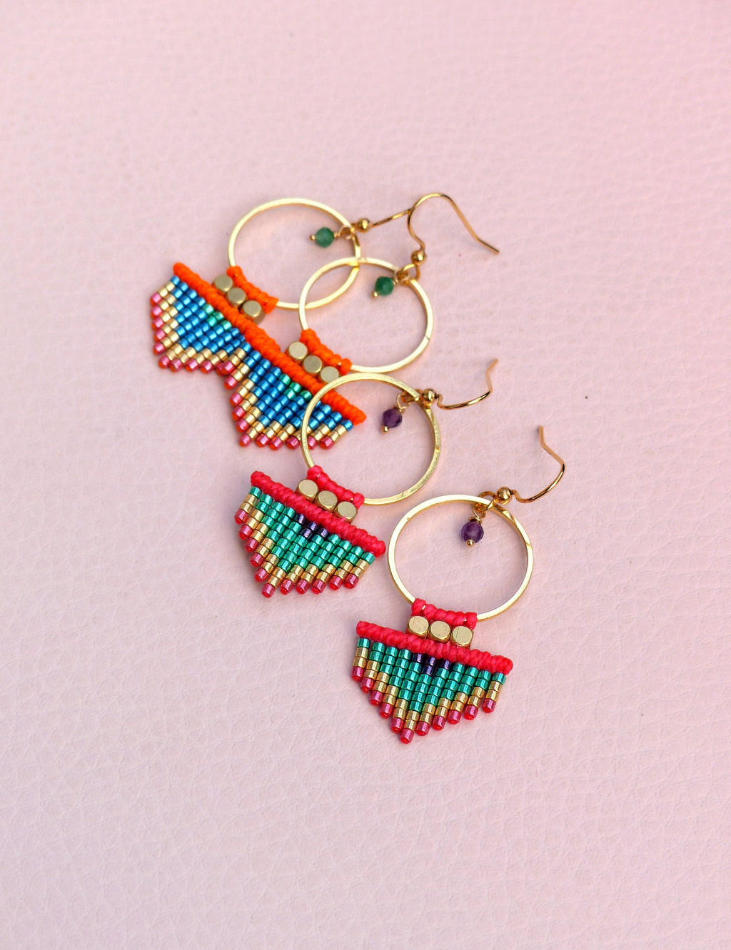 Peut inclure: Une paire de boucles d'oreilles créoles dorées avec des franges de perles colorées. Les franges sont composées de petites perles colorées dans des tons de rouge, vert, bleu et or. Les boucles d'oreilles sont un accessoire unique et élégant.