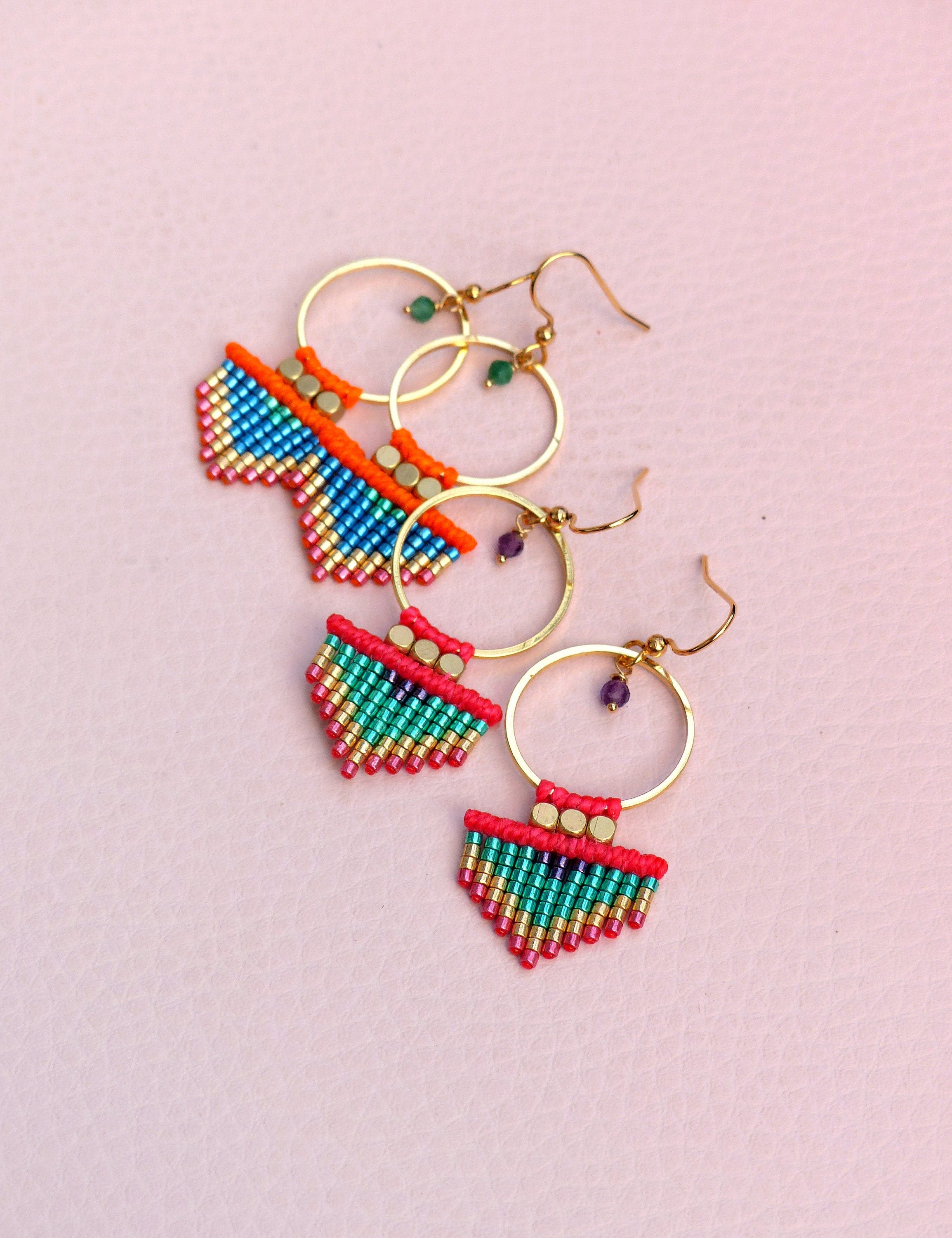 Peut inclure: Une paire de boucles d'oreilles créoles dorées avec des franges de perles colorées. Les franges sont composées de petites perles colorées dans des tons de rouge, vert, bleu et or. Les boucles d'oreilles sont un accessoire unique et élégant.