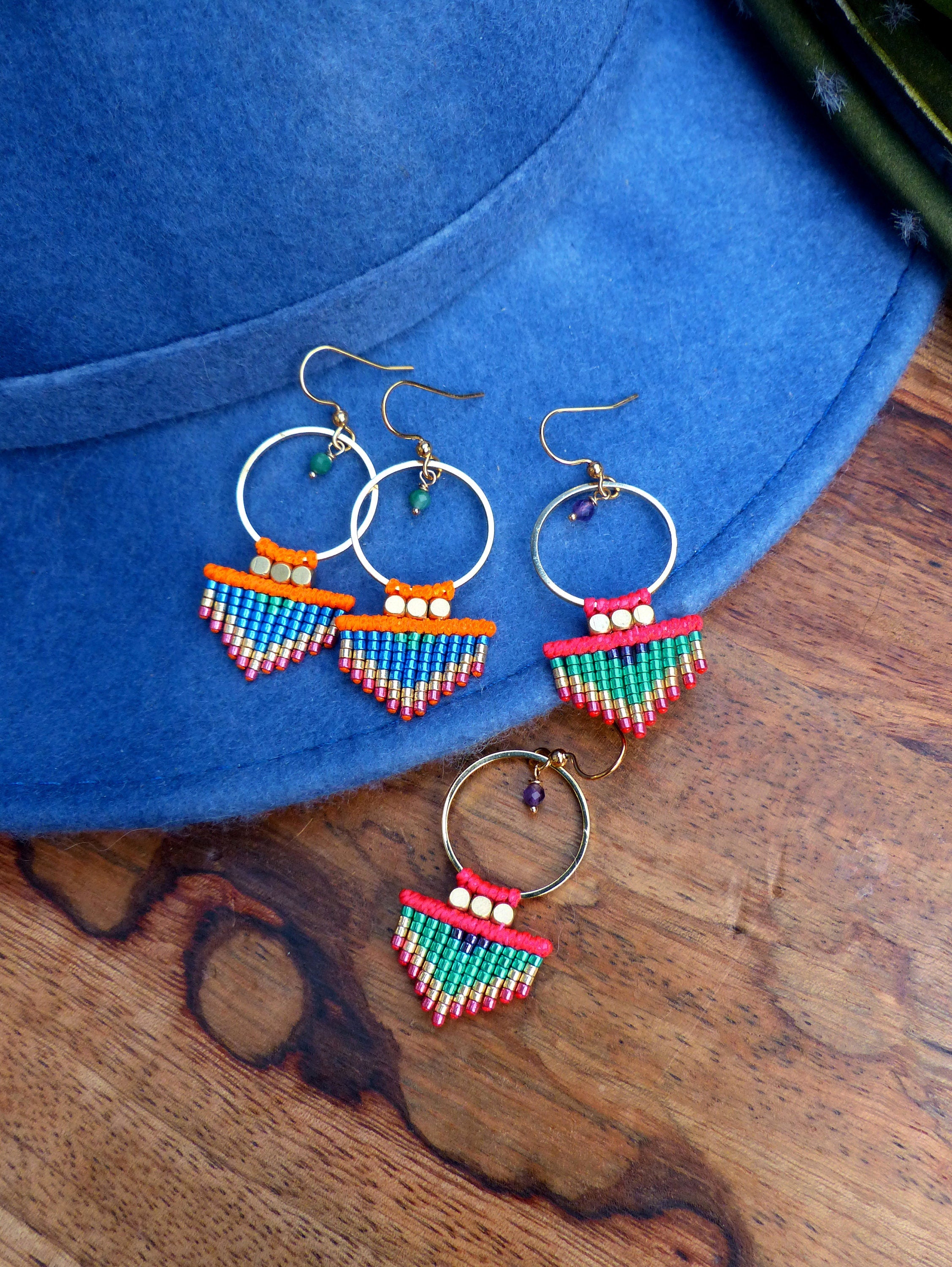 Peut inclure: Trois paires de boucles d'oreilles en perles colorées avec des cercles dorés. Les boucles d'oreilles présentent un design en frange avec des perles rouges, orange, vertes et bleues.