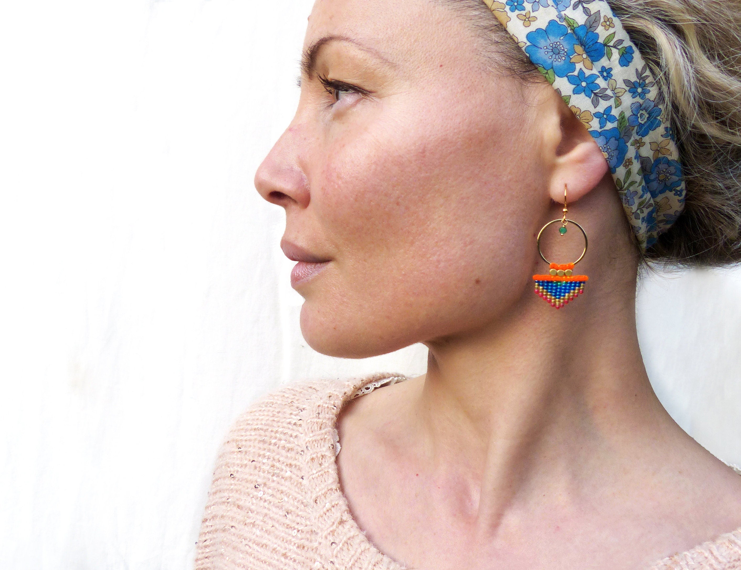 Peut inclure: Une paire de boucles d'oreilles créoles dorées avec un pendentif géométrique en perles bleues, orange et vertes.