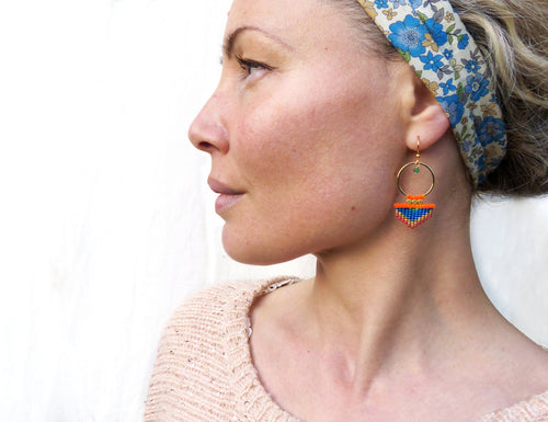 Peut inclure: Une paire de boucles d'oreilles créoles dorées avec un pendentif géométrique en perles bleues, orange et vertes.