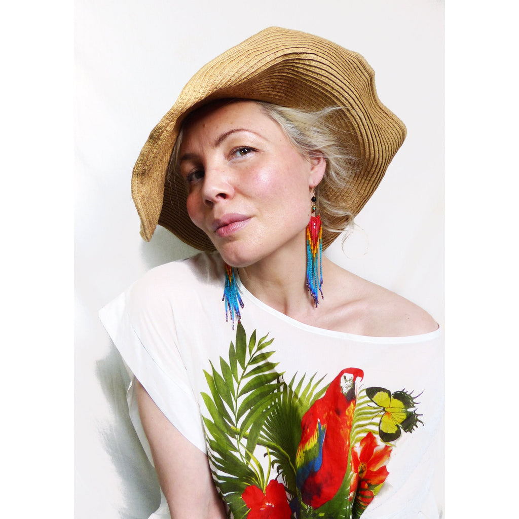 Peut inclure: Une femme portant un chapeau de paille et une chemise blanche à imprimé tropical. Elle porte de longues boucles d'oreilles en perles colorées.