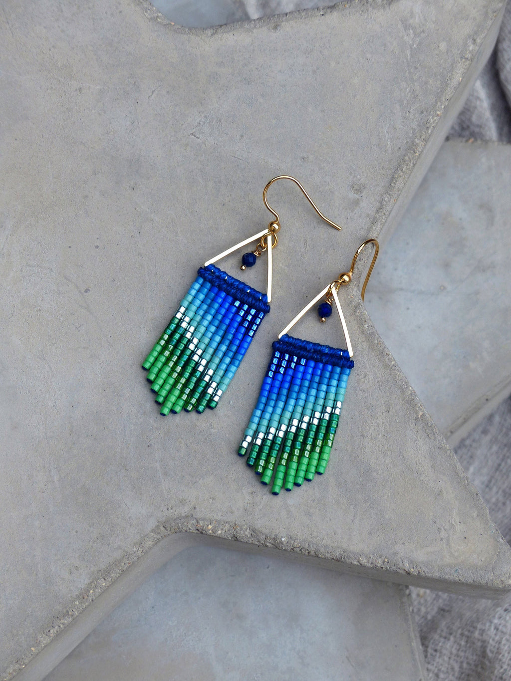 Peut inclure: Une paire de boucles d'oreilles pendantes en triangle doré avec des franges de perles bleu et vert dégradées.