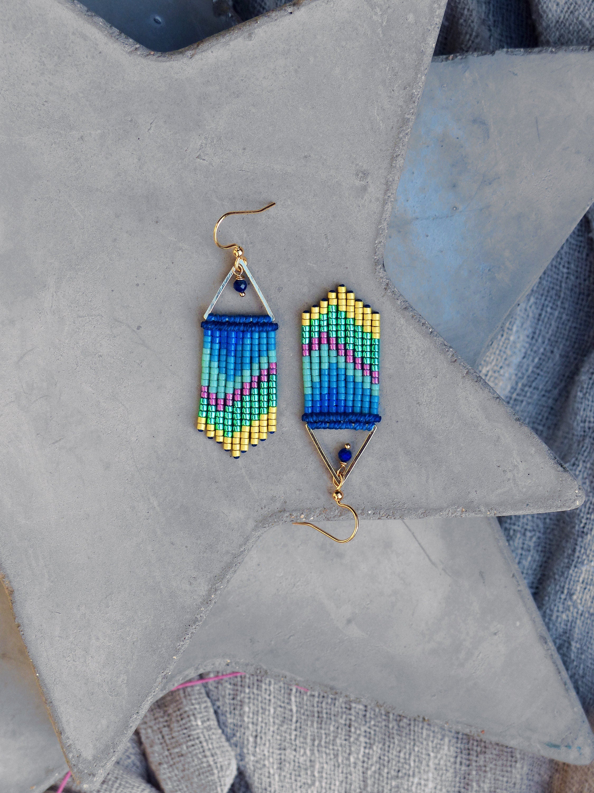 Peut inclure: Une paire de boucles d'oreilles pendantes avec un motif géométrique. Les boucles d'oreilles sont faites de perles bleues, vertes et jaunes et ont une finition dorée.