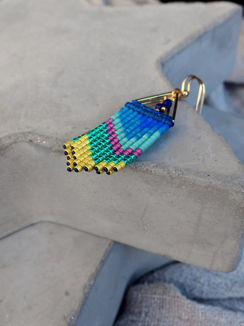 Peut inclure: Une paire de boucles d'oreilles pendantes avec un design géométrique. Les boucles d'oreilles sont faites de perles bleues, vertes, jaunes et roses. Les boucles d'oreilles sont attachées à un crochet doré.