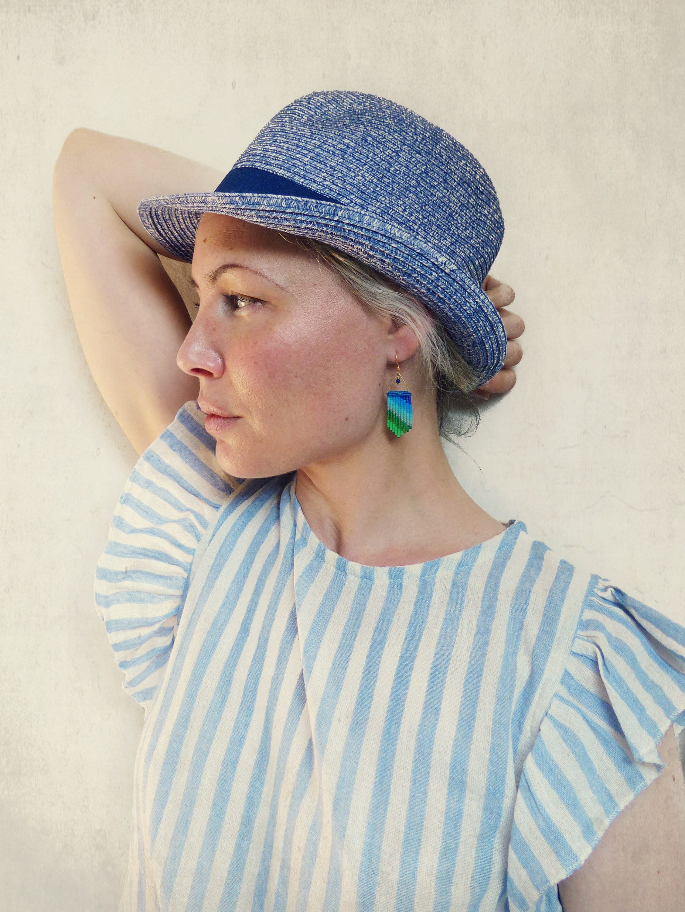Peut inclure: Une femme portant une chemise à rayures bleues et blanches avec des manches bouffantes et un chapeau bleu. Elle porte une paire de boucles d'oreilles dégradées vertes et bleues.