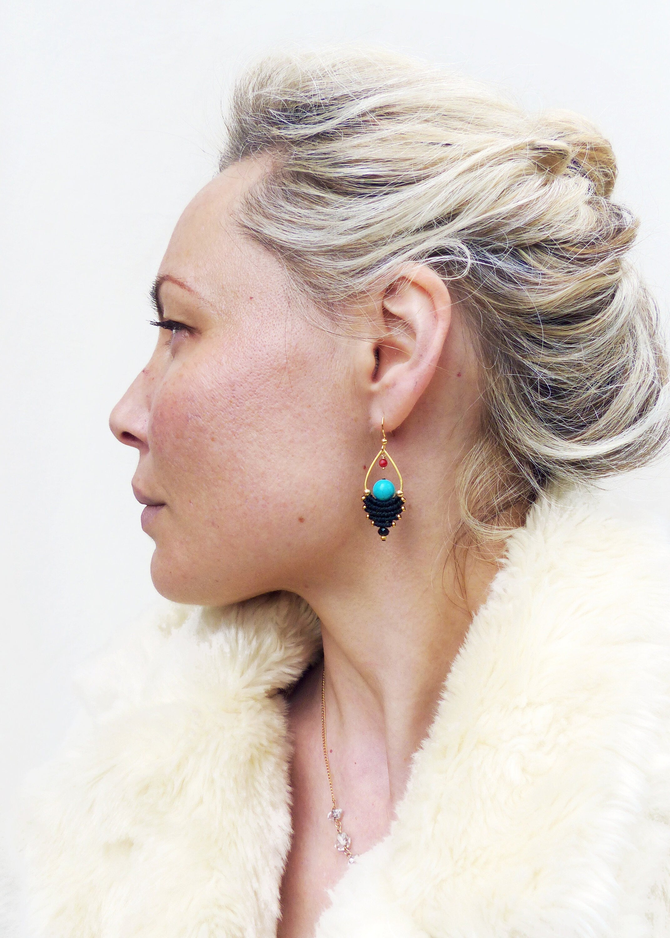 Peut inclure: Une femme portant une veste en fourrure blanche avec un collier en or et des boucles d'oreilles pendantes turquoise et noires.