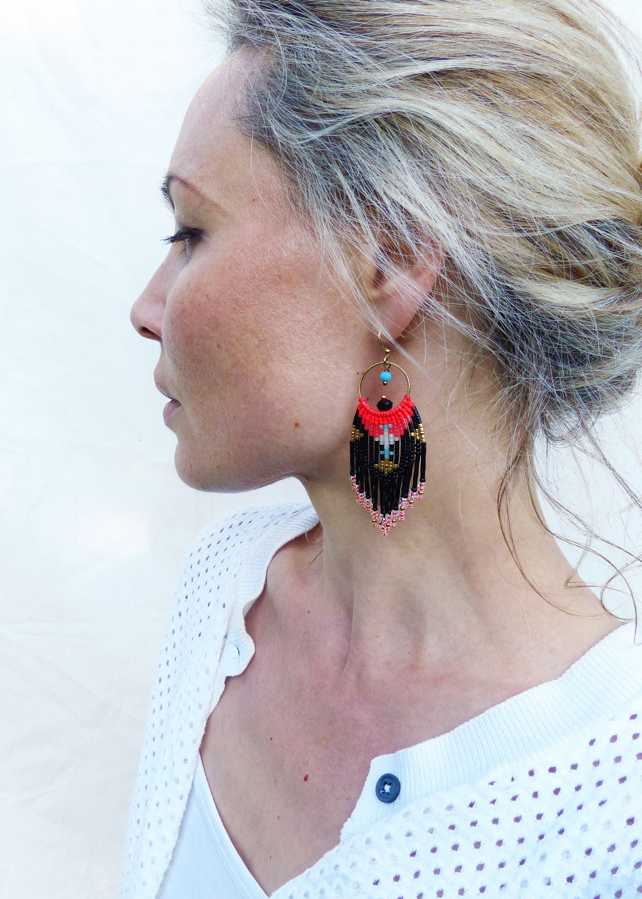 Peut inclure: Une paire de boucles d'oreilles pendantes avec un motif de perles noires, rouges et dorées. Les boucles d'oreilles sont faites de petites perles et ont un bas en forme de frange.