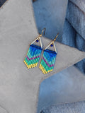 Peut inclure: Une paire de boucles d'oreilles pendantes en forme de triangle doré avec des franges de perles bleues, vertes, jaunes et roses.